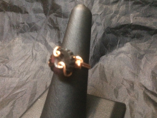 A deep garnet colored 12mm round Czech pressed glass bead  cut with a daisy pattern is set with swirls and coils in this copper wire wrapped ring. Rings made by this wire wrapping method vary individually. This one is approxmately a size 6.5.