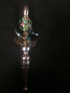The design theme for this bottle stopper uses plated metal and glass leaves to form base of a flower bush represented by a large glass bead.åÊ The cental stalk of the bush uses more metal beads.