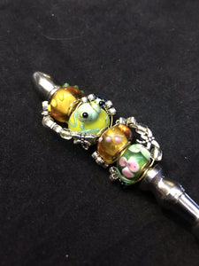 A blown glass bead with a raised glass frog peeks out from the lagoon at dainty metal dragonflies swirling around the handle of this butter knife.
