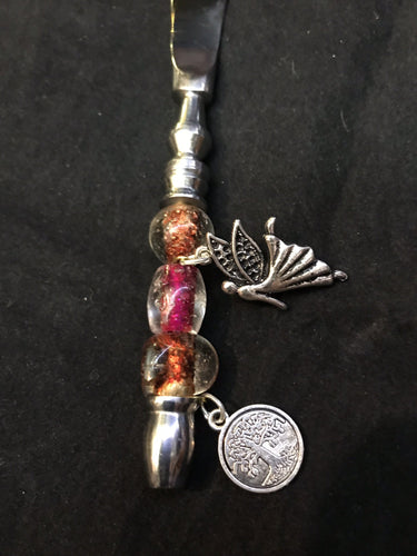 A fairy charm flies across rosy pink blown glass beads toward her home tree on this butter knife handle.