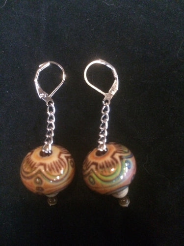 A pair of drum shaped mood beads that change color with temperature sit on a silver plated chain below silver plated brass leverbacks.