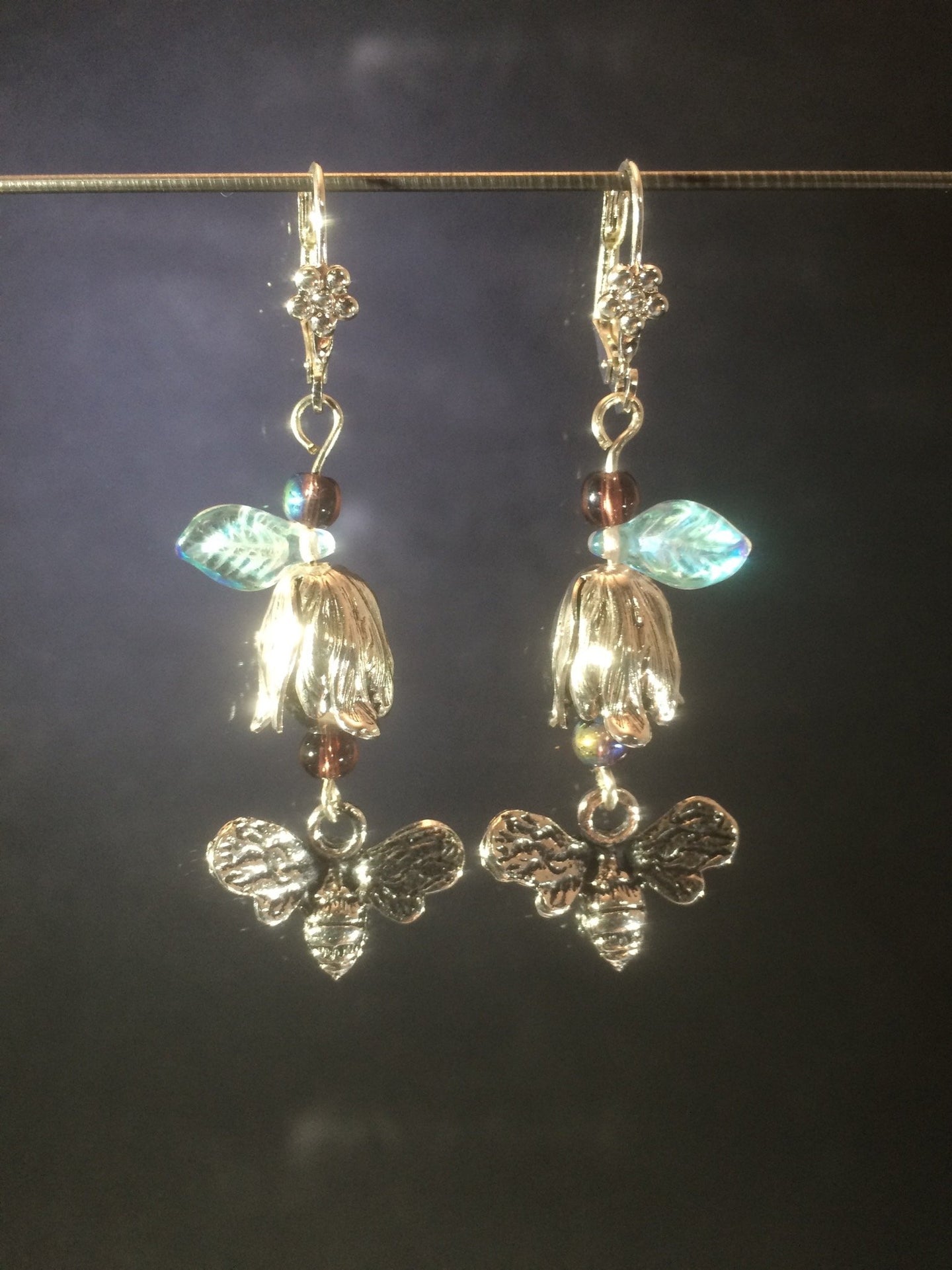 These leverback earrings feature silver plated zinc petwer charms of bees and flowers along with Czech pressed glass leaves and glass pearls.