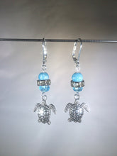 Load image into Gallery viewer, Leverback earrings with metal sea turtle charms, blue colored and faceted glass beads, and a faceted crystal cluster.
