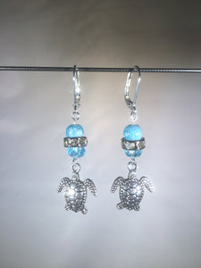 Leverback earrings with metal sea turtle charms, blue colored and faceted glass beads, and a faceted crystal cluster.