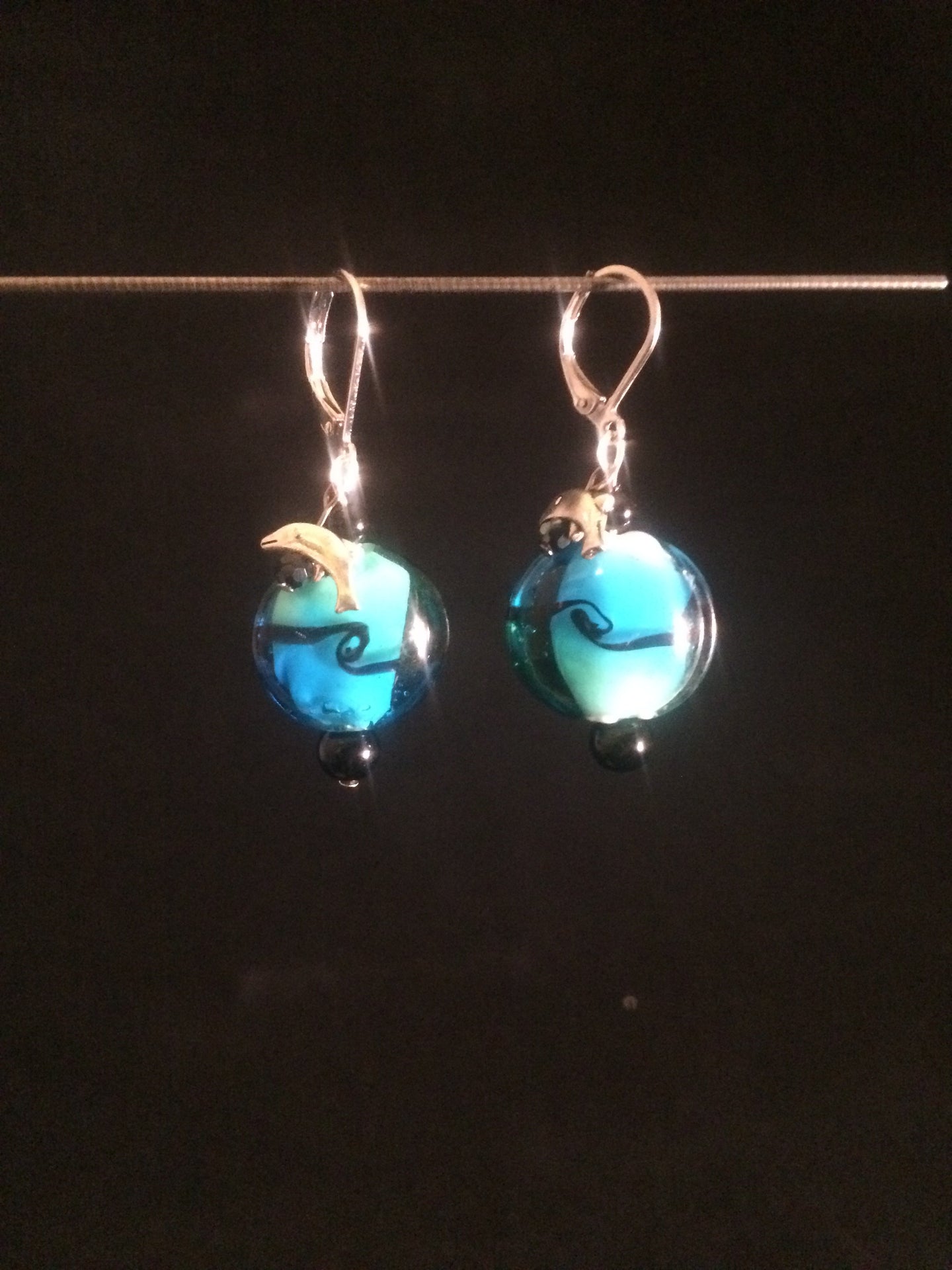 Leverback earrings made with a blue blown glass bead and adorned with a plated metal charm of either a fish, dolphin, or a shell.  Faceted and round glass beads are added for accent.