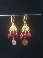 Load image into Gallery viewer, Leverback chandelier earrings adorned with red glass beads and a metal leaf charm.