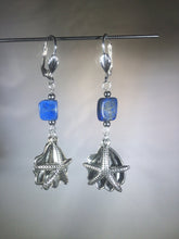 Load image into Gallery viewer, Metal sea star (starfish) and oyster charms dangle below a vibrant blue 8mm lapis lazuli bead in these silver plated brass leverback earrings. 
