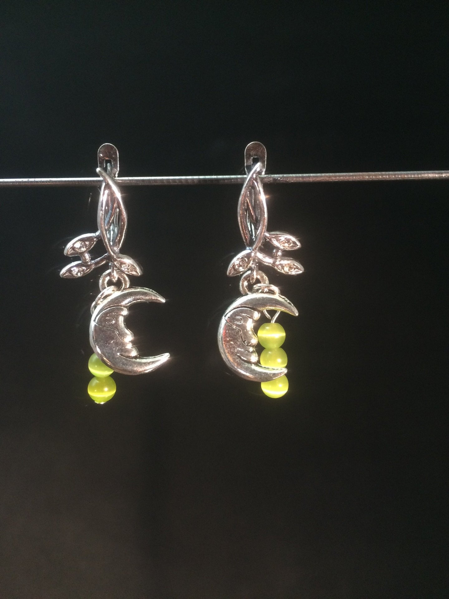 A silver plated moon charm is adorned with natural peridot beads, then set on silver plated brass leverbacks. These earrings form a matching set with necklace 1NCK0053.