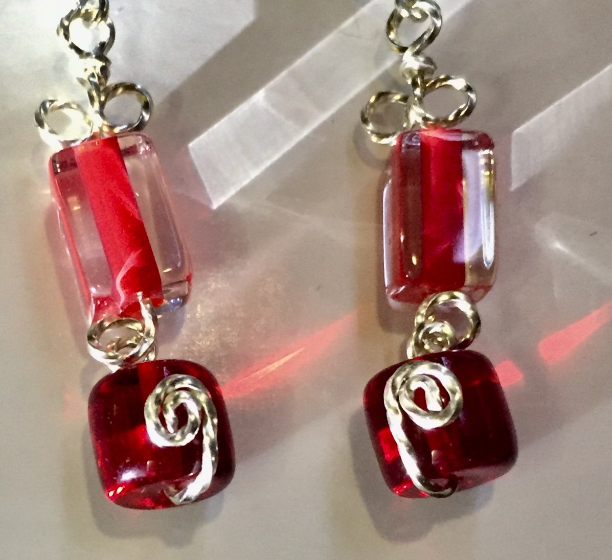 Red glass beads form geometric patterns in rectangles and cylinders, with swirly silver wire looped in between on these leverback silver earrings.
