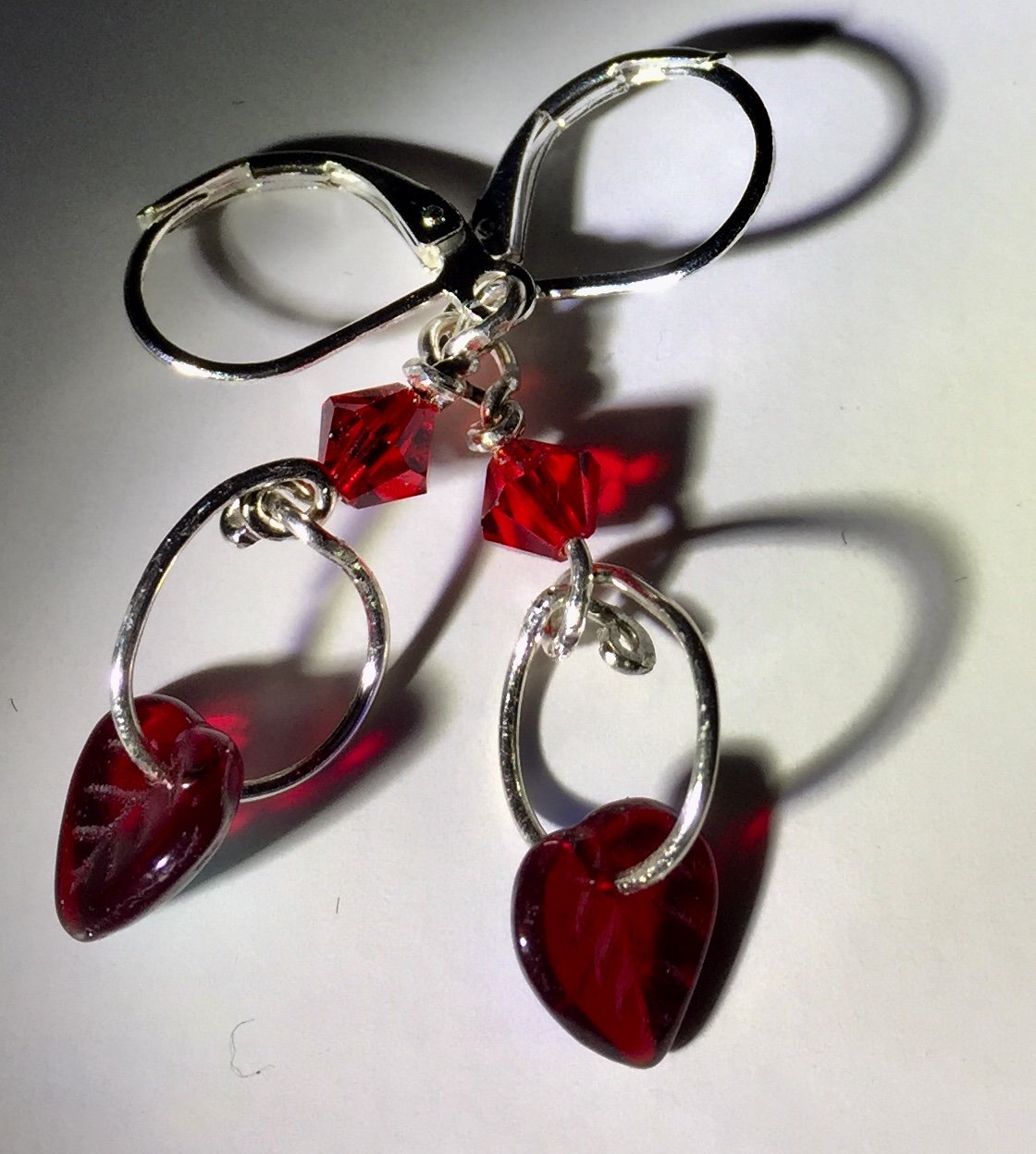 Delicate fine silver loops hold dangling irridescent red glass heart shaped leaf beads below a shiny red Swarovski bicone in these silver leverback earrings. The backs of the glass leaves are irridescent blue, giving them extra shimmer as they rustle with your movement!