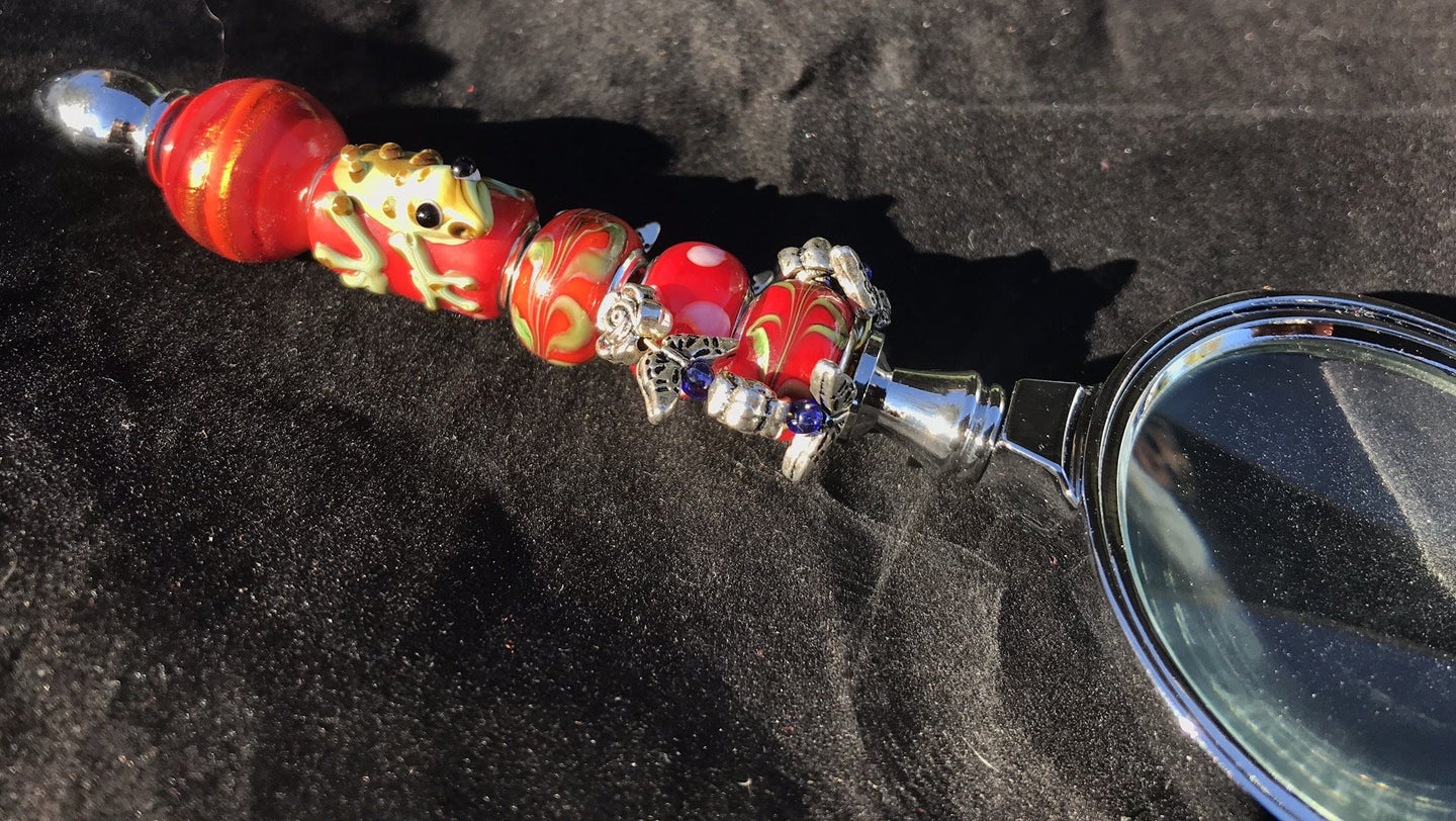 Blown glass beads featuring a raised frog peek out among leafy and flowery charms on the handle of this magnifying glass.