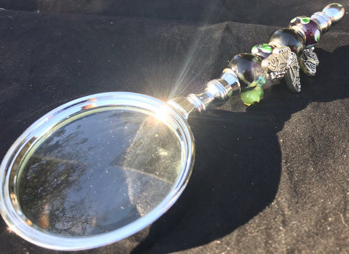 Tiny blown glass frogs peek out from underwater amongst swirling columns of butterflies against a backdrop of night garden blown glass beads on the handle of this magnifying glass.