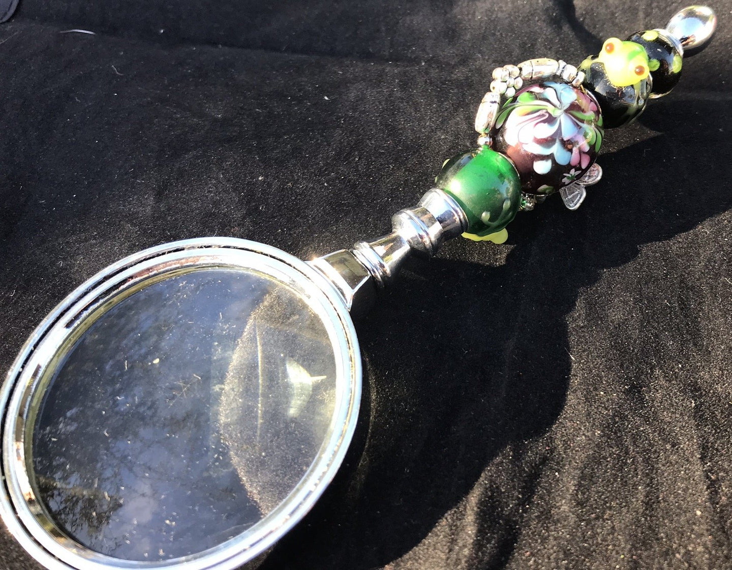 Tiny blown glass frogs appear to be climbing toward a central flowery blown glass bead, accented by viney rose charms, on the handle of this magnifying glass.