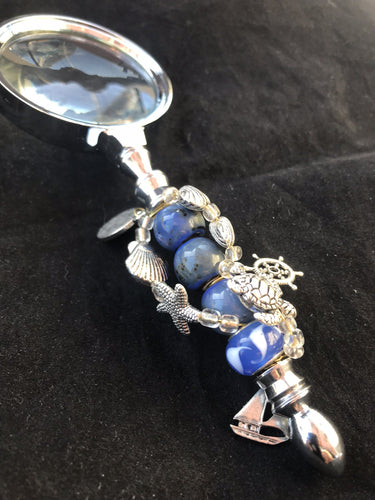 An anchor charm dangles over sea life charms and dazzling blue cut and blown glass beads on the handle of this magnifying glass.
