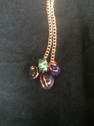 Three amethyst beads surround a green and white agate bead in a design meant to be evocative of a cluster of grapes, with the swirling copper wire wrap evoking images of the vine. The pendant is set on a 22