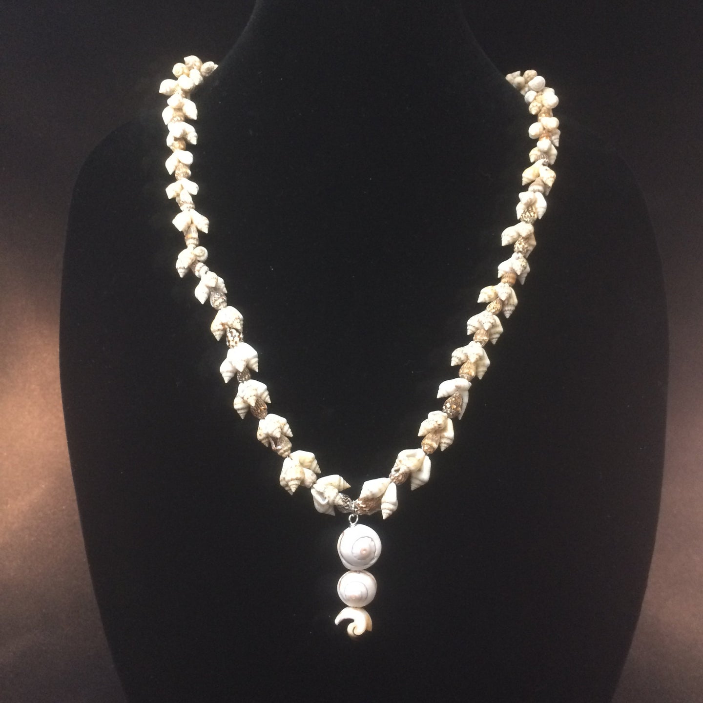 This necklace has clusters of light snail shells with a pendant made from segments of larger shells.