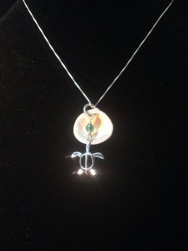 A necklace made from a sterling silver sea turtle charm along with a real clam shell background and a glass bead accent, mounted on an 18