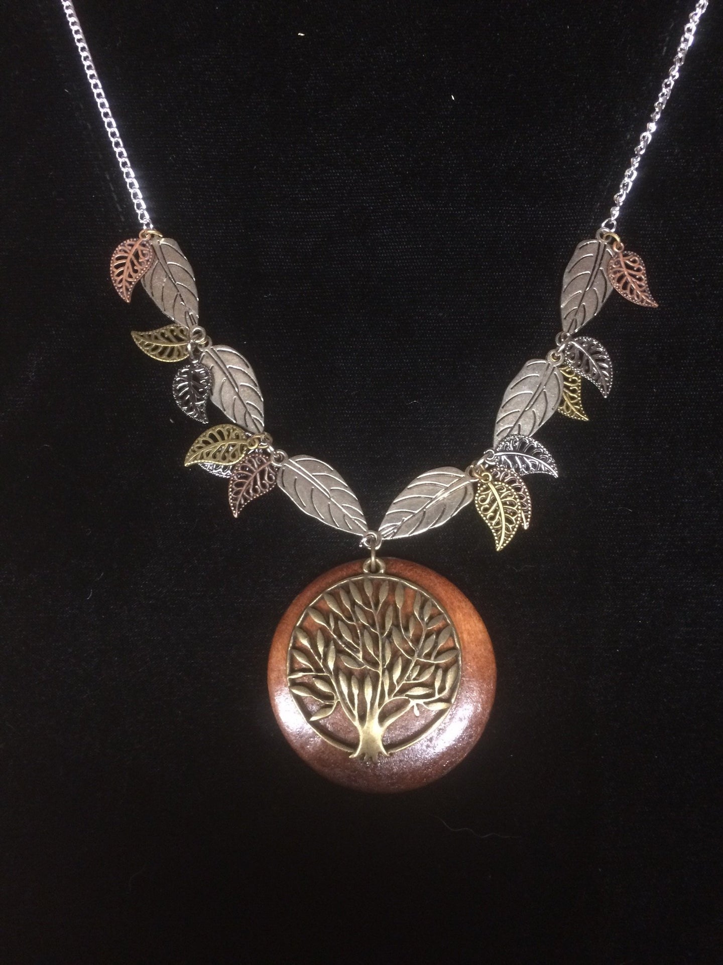 In this necklace, a wooden disk backs aåÊmetal tree of life pendant with metal leaves of different finishes and sizes surrounding it on the 18