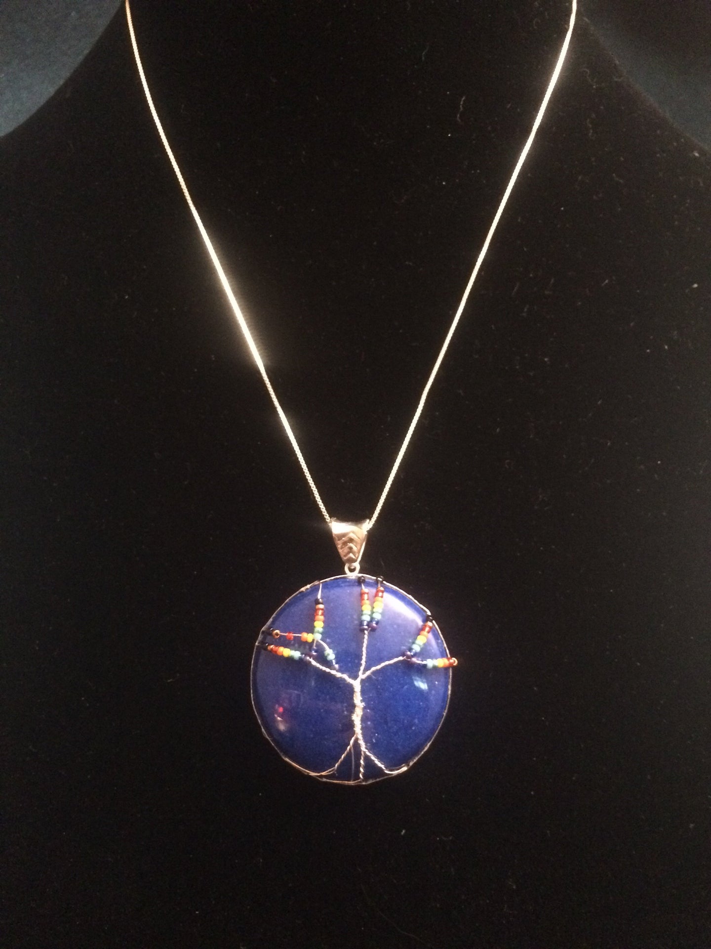 This tree of life uses the inclusive rainbow as the color theme made with glass seed beads on fine silver wire on a silver chain. The background is a cabochon of Mountain Jade (dolomite marble) which has been dyed to its color.