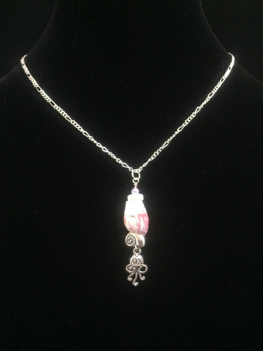 A barnacle sourced locally in St. Augustine Beach is accented by silver plated charms and glass beads, then mounted on a 16