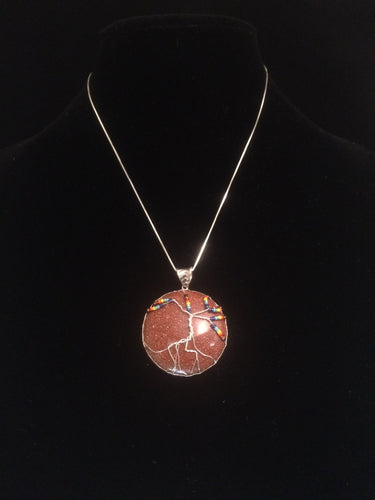 This tree of life uses the inclusive rainbow as the color theme made with glass seed beads on fine silver wire on a silver chain. The background is a 30mm cabochon of lab created sunstone in gold.