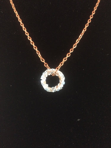 Tiny blue topaz faceted gems are mounted on a brass ring, with a copper chain passing through it.