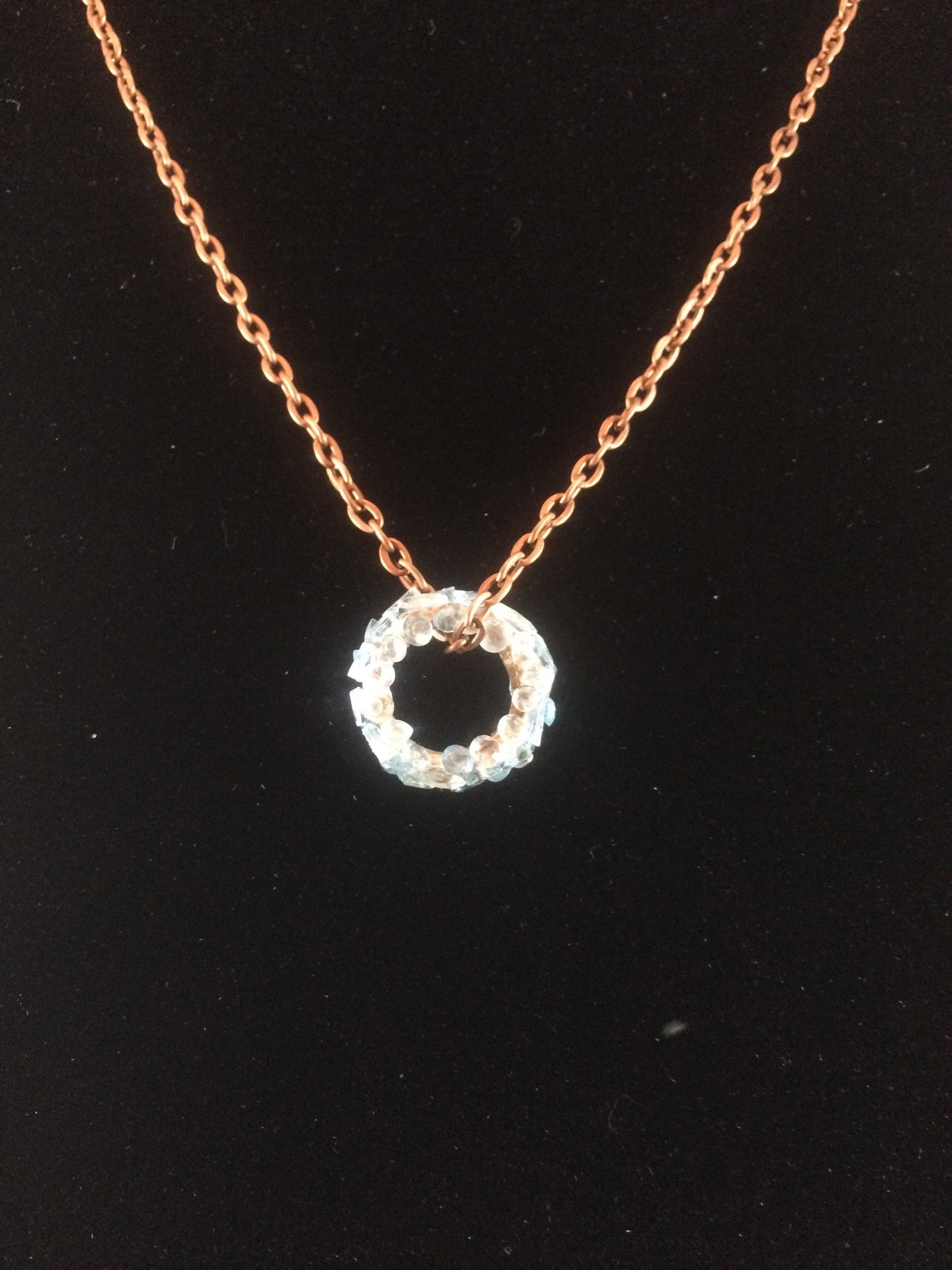 Tiny blue topaz faceted gems are mounted on a brass ring, with a copper chain passing through it.