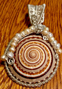 A 2" diameter cone snail shell is wrapped in woven fine silver and accented with freshwater cultured pearls to form this pendant. The pendant is mounted on a 16" sterling silver chain, so that the shell sits right at the collarbone. The wire weave extends to the back of the shell, ensconcing the shell's opening--you can see right down into the shell's interior!