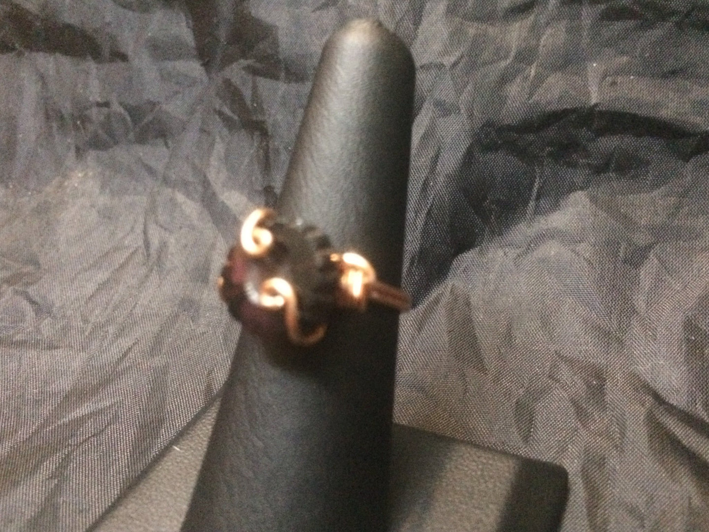 A deep garnet colored 12mm round Czech pressed glass bead  cut with a daisy pattern is set with swirls and coils in this copper wire wrapped ring. Rings made by this wire wrapping method vary individually. This one is approxmately a size 6.5.