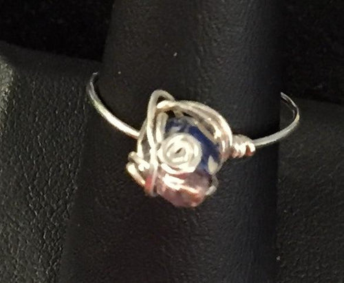 A 6mm reconstituted and dyed shell round bead is set with a swirl and a purple glass seed bead into this sterling silver wire wrapped ring. Rings made by this wire wrapping method vary individually. This one is approxmately a size 8.