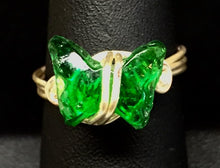 Load image into Gallery viewer, A green glass butterfly bead forms the focal of this silver plated copper wire wrapped ring. Rings made by this wire wrapping method vary individually. This one is approxmately a size 6.75, but may fit a slightly larger finger depending on how snug a fit you prefer.